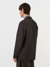 A model is wearing the Brown Marl Tropical Suiting Two Button Jacket against a plain white background. The image is taken from a rear-side perspective, showing the back of the jacket, its structured shoulders, and the fit of the sleeves. The brown marl fabric is prominent. No mannequin is present.