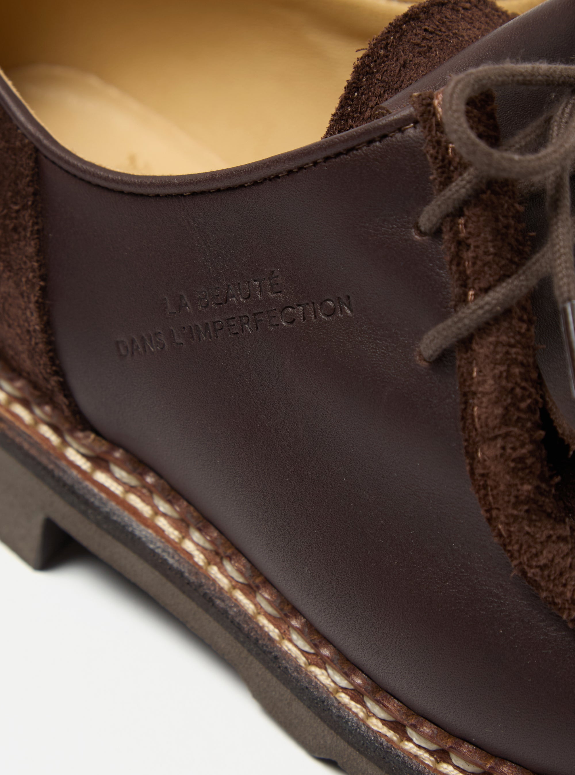 Close-up of the Paraboot x Universal Works Michael in Coffee Leather/Suede. Features brown leather and suede, with visible stitching on a white surface. "LA BEAUTE DANS L'IMPERFECTION" embossed.