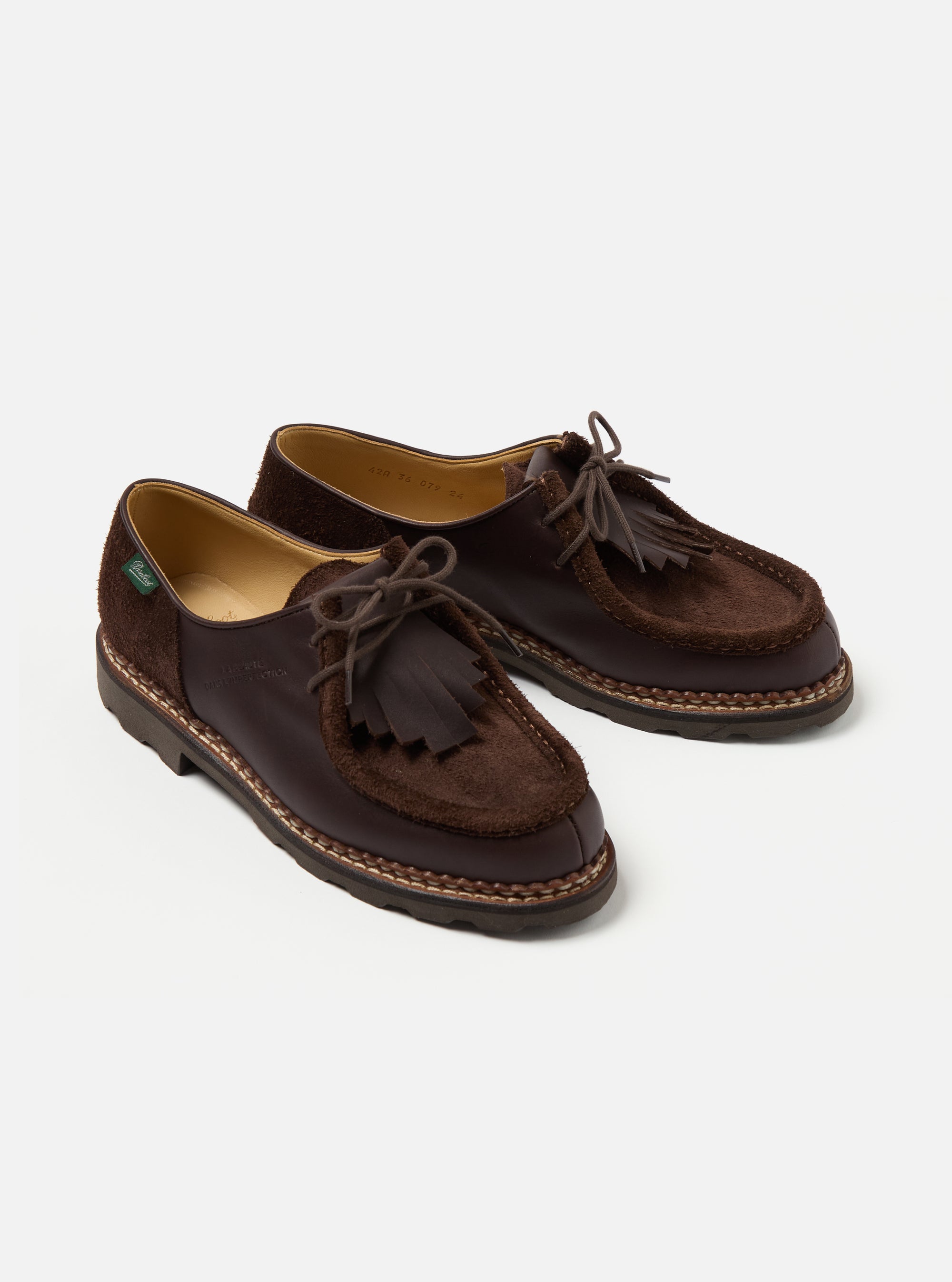 Paraboot x Universal Works Michael shoes in coffee leather and suede on a white background. The shoes have a moccasin style with tassels and lace-up closure.