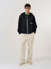 A model wears the Navy Cotton Recycled Nylon Mix Daley Jacket against a plain white background. The jacket is a deep navy blue hoodie with a full-zip front, a drawstring hood, and two large patch pockets at the waist. The model is shown from the waist up, facing forward with the jacket fully zipped.