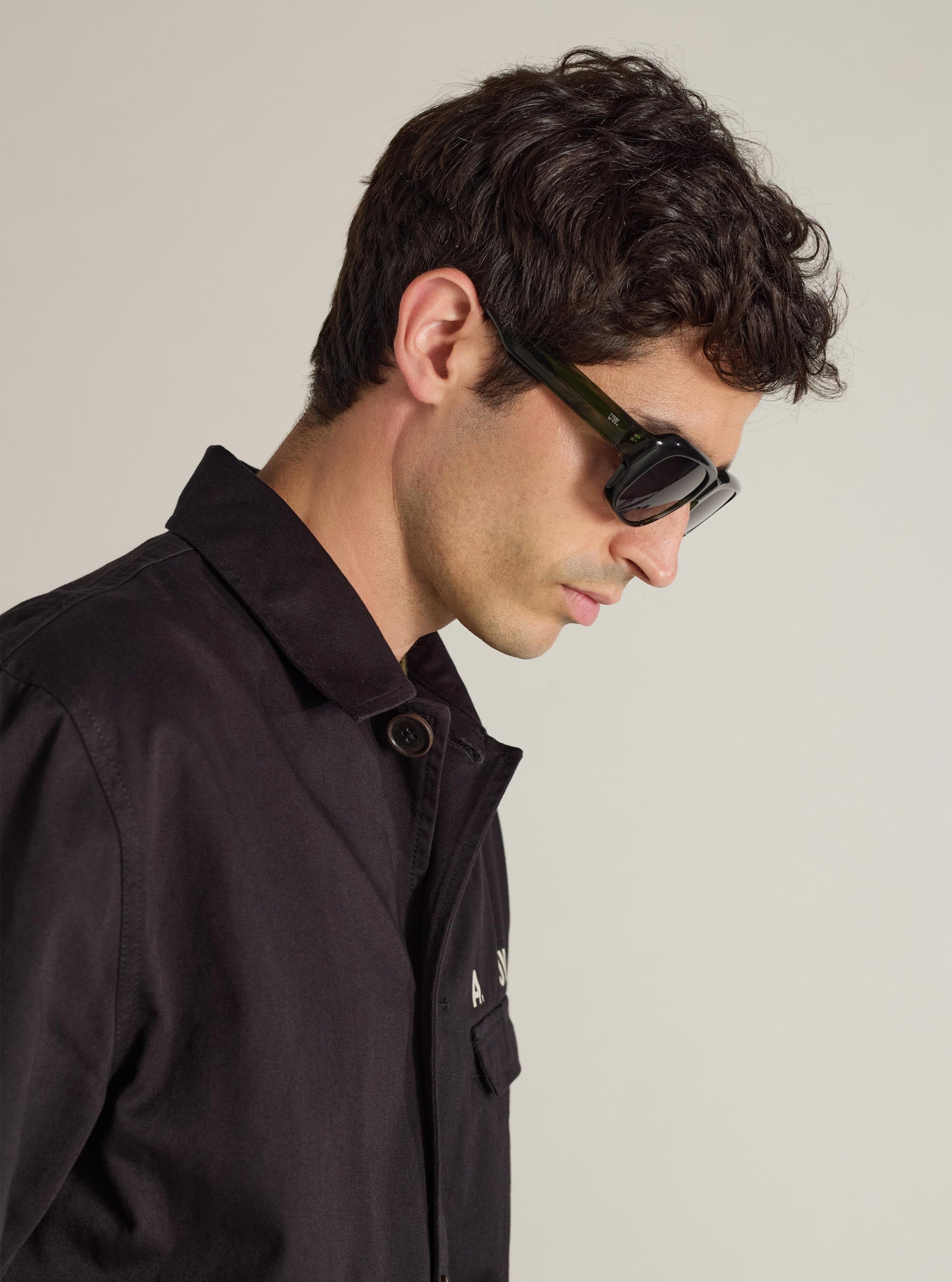 A model showcases A. SOCIETY x Universal Works Green Aberdeen Sunglasses. The sunglasses have a green frame. Shot in a studio with a plain background.