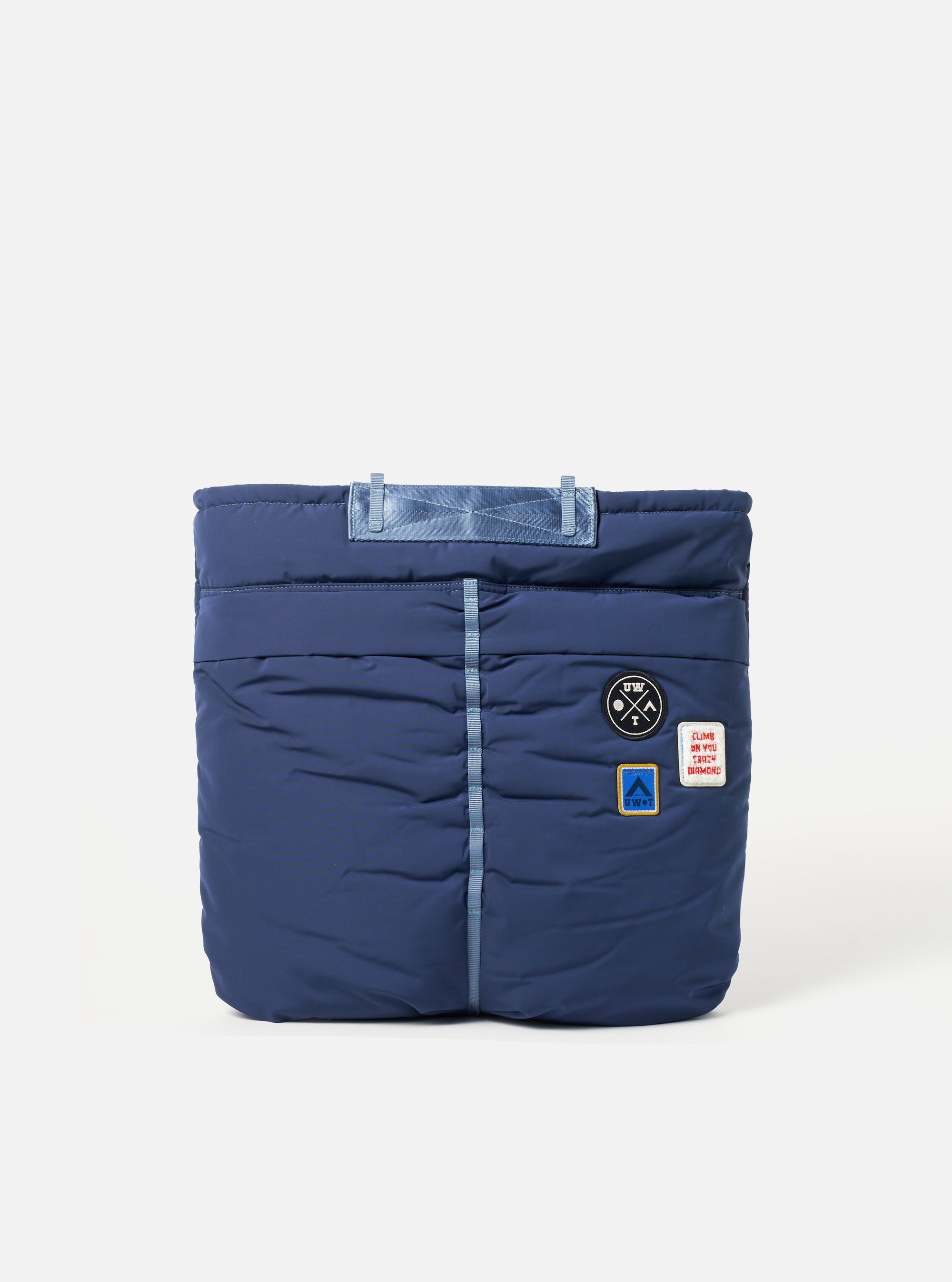 The Topologie x Universal Works Insignia Blue UW Tech Helmet Bag. Padded blue bag with UW patches. Studio shot on white backdrop.