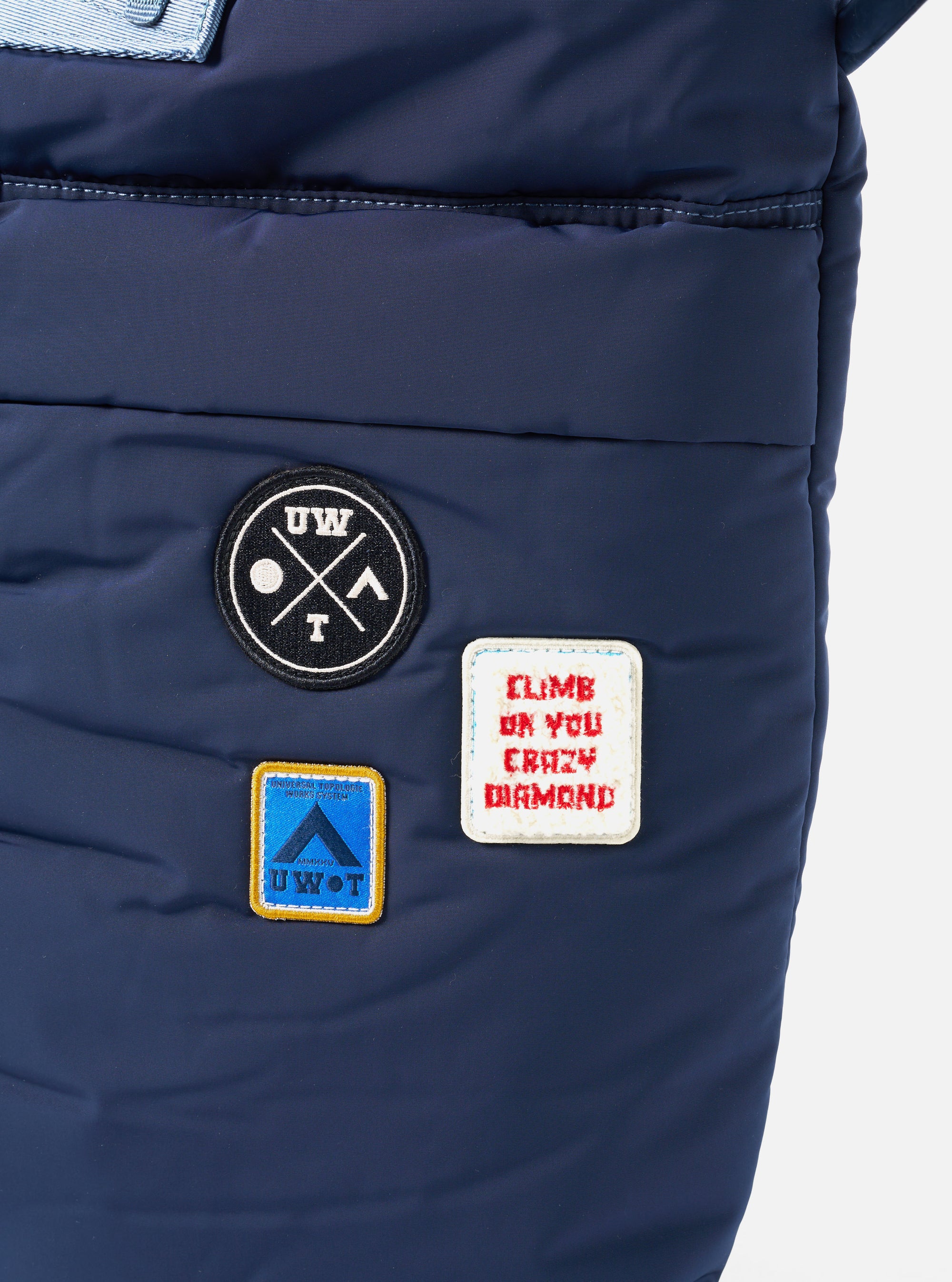 Close-up of the Topologie x Universal Works Insignia Blue UW Tech Helmet Bag. Features patches on the blue material. Shot against a white backdrop.