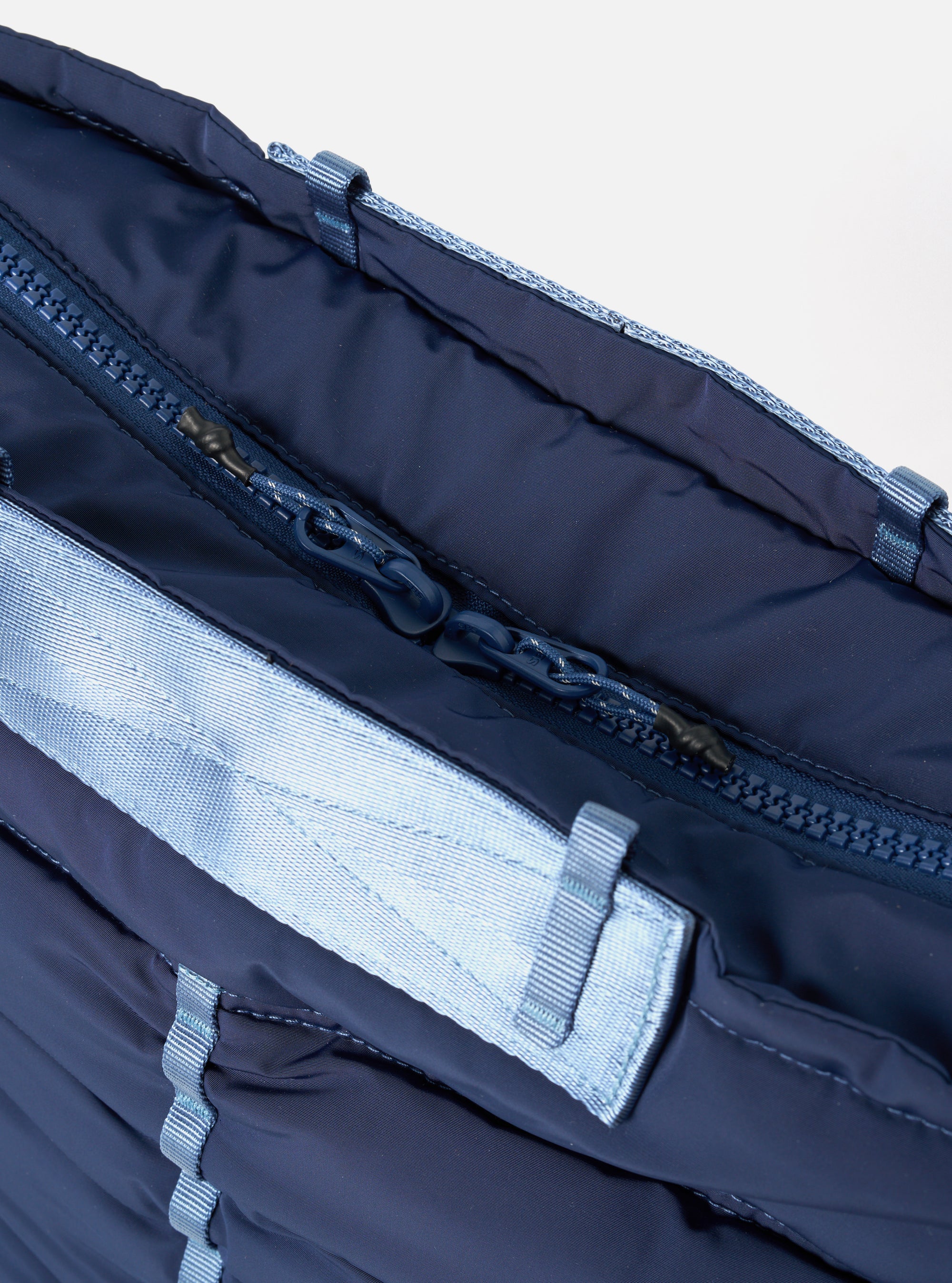 Close-up of the Topologie x Universal Works Insignia Blue UW Tech Helmet Bag. Shows the bag's blue fabric, zipper, and light blue straps against a white backdrop.