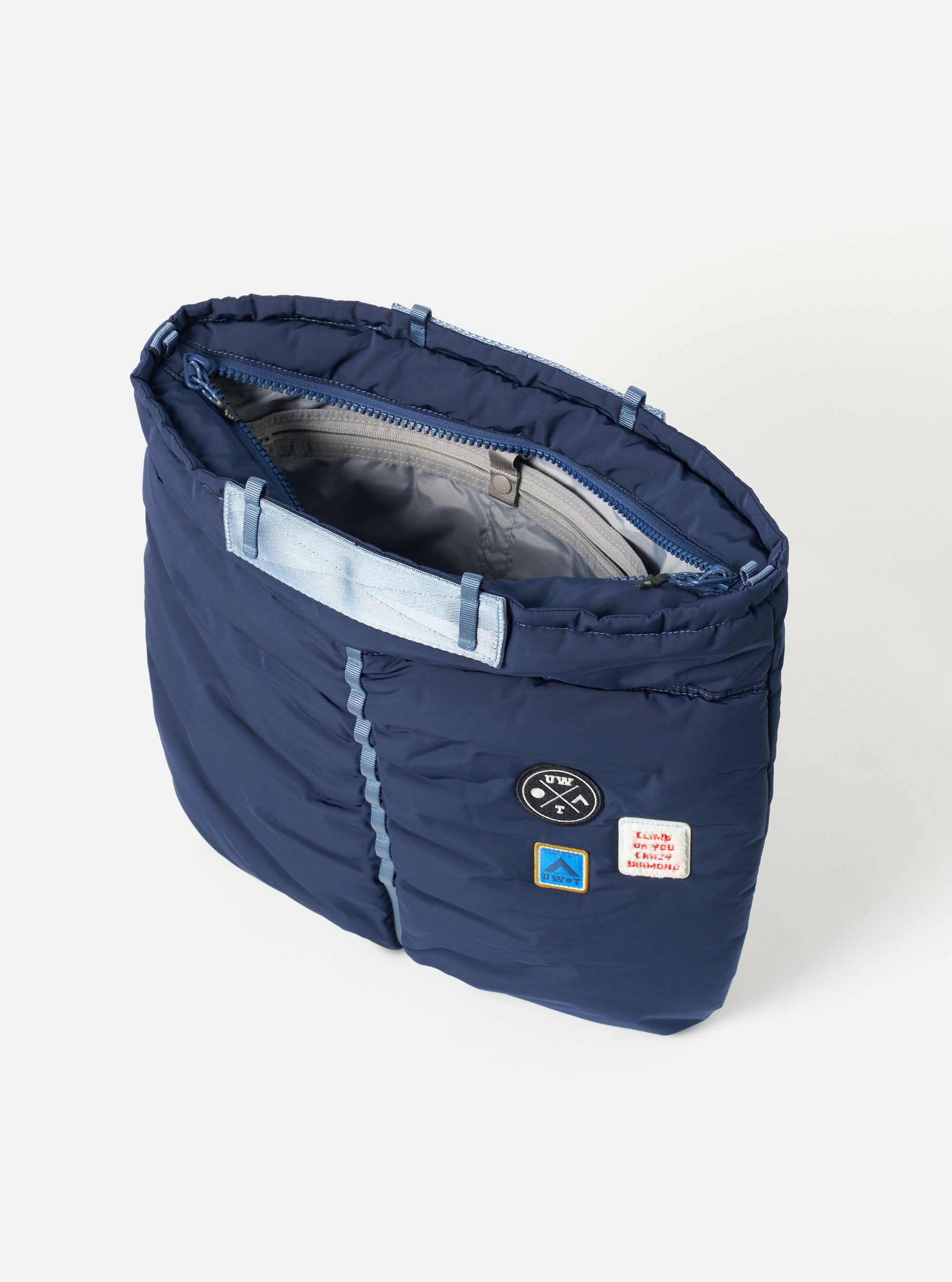 Topologie x Universal Works Insignia Blue UW Tech Helmet Bag on a white background. The bag is navy with light blue straps and patches.