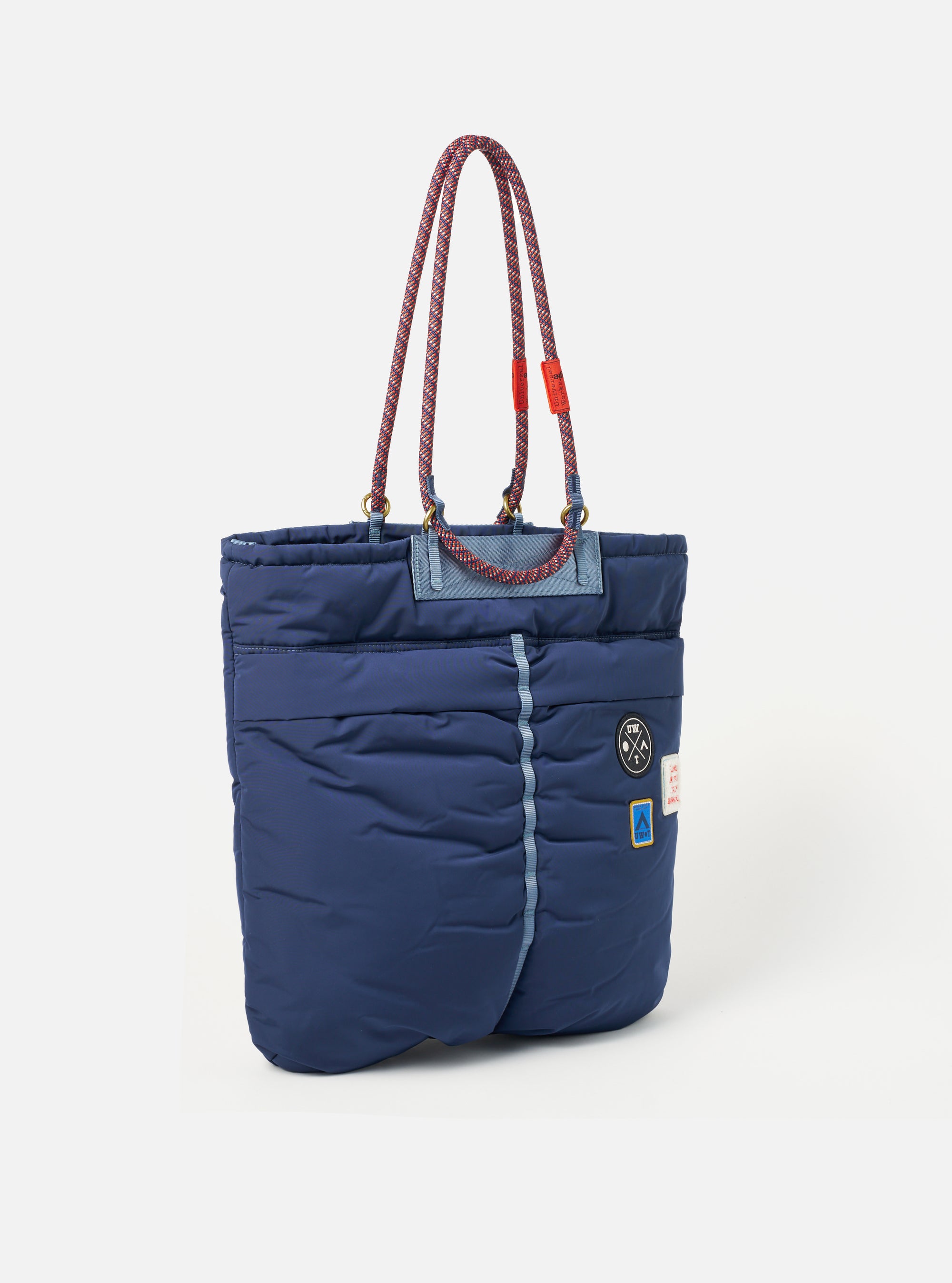 Topologie x Universal Works Insignia Blue UW Tech Helmet Bag on a white background. The bag is puffy with rope handles and small logo patches.