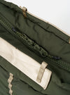 Close-up of the Topologie x Universal Works Rifle Green UW Tech Helmet Bag. Features a green zipper, olive green fabric, and beige straps. Shot on a white background.