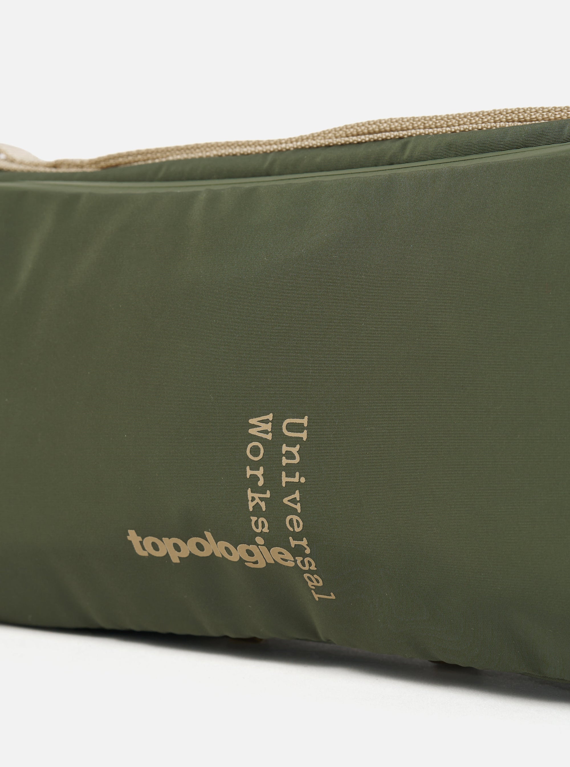 Close-up of the Topologie x Universal Works Rifle Green UW Tech Bottle Sacoche Medium. Features olive green material with beige straps and logo detailing on a white background.