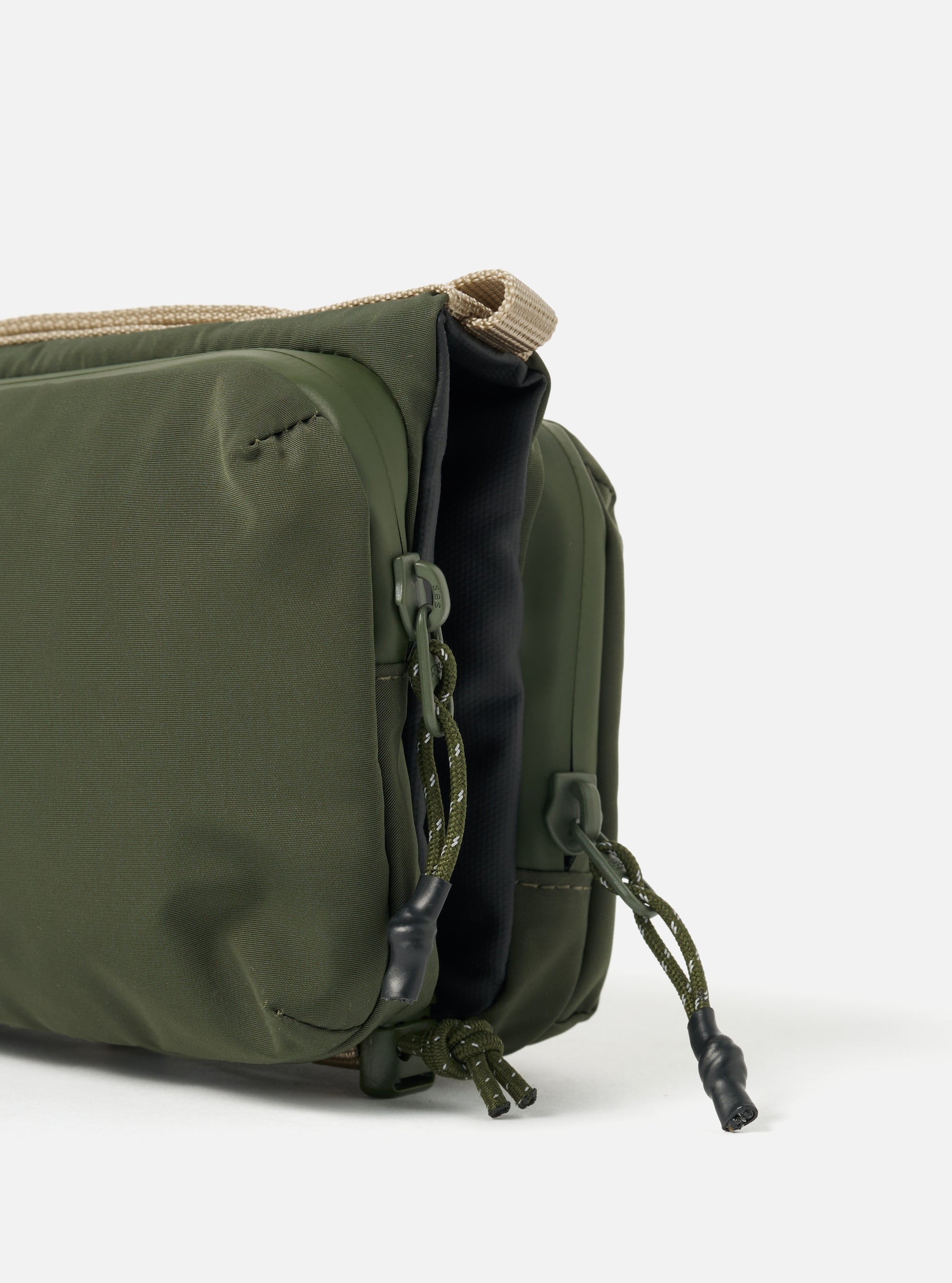 Close-up of the Topologie x Universal Works Rifle Green UW Tech Bottle Sacoche Medium on a white background. Shows the green material, beige strap, and zipper pulls.