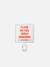 Close-up of the Topologie x Universal Works Off White UW Tech Phone Strap Adapter. Features an off-white fabric with red text and a blue border, paired with a silver metal loop on a white background.