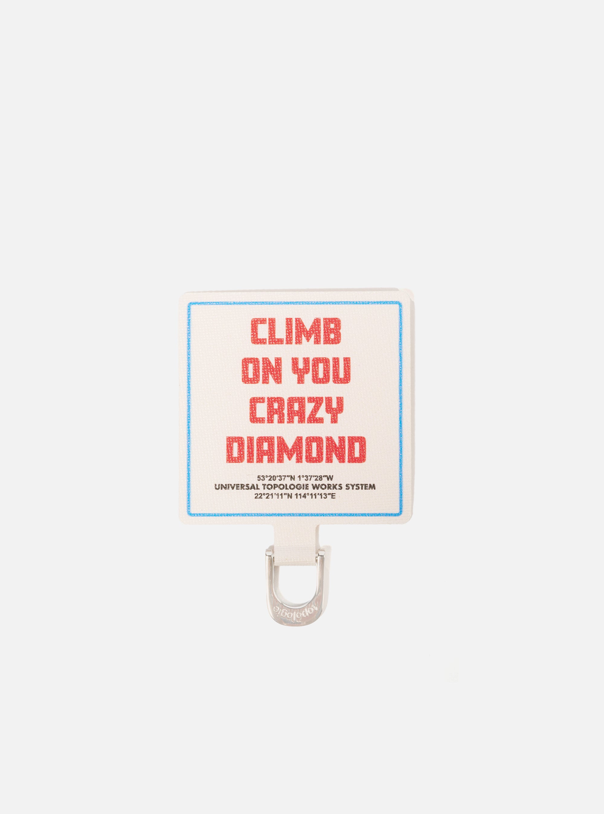 Close-up of the Topologie x Universal Works Off White UW Tech Phone Strap Adapter. Features an off-white fabric with red text and a blue border, paired with a silver metal loop on a white background.