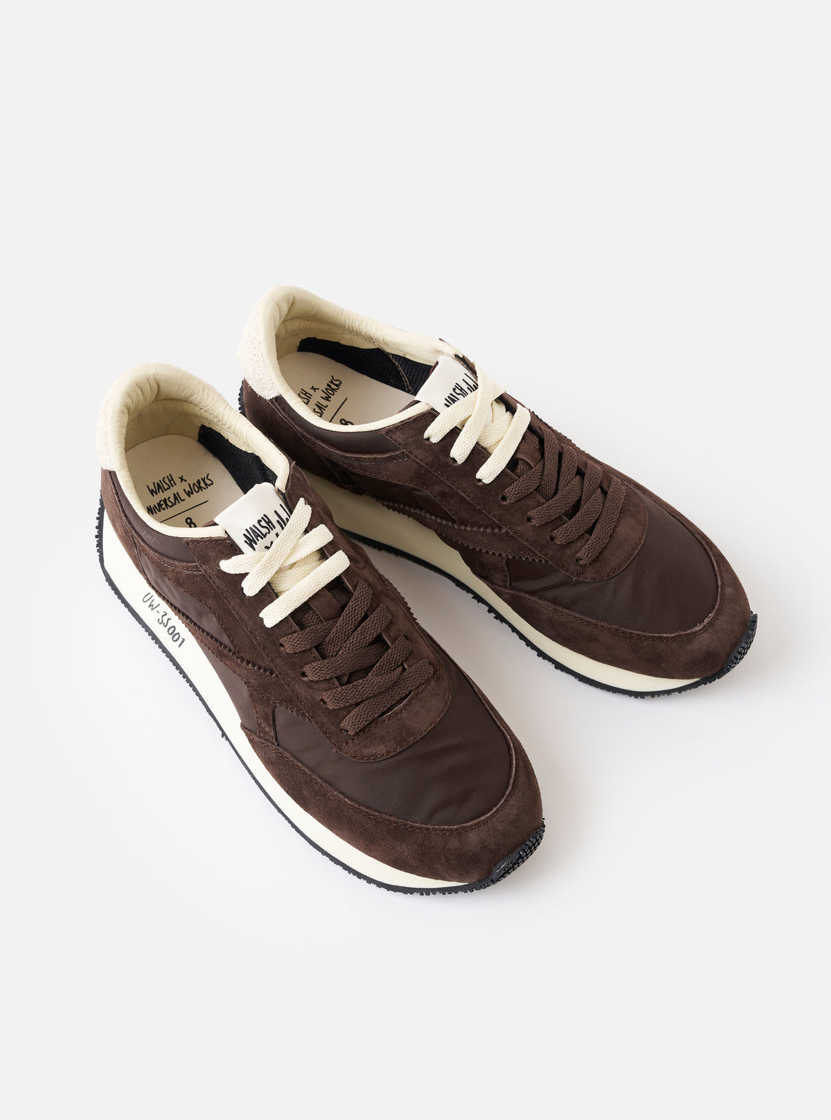 A close-up view of the heel and back tab of the Walsh x Universal Works Tornado sneaker in brown leather and canvas against a white background, detailing the fine stitching, collar padding, and rear sole profile.