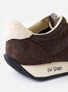 A bottom view showing the tread pattern of the Vibram rubber outsole on the Walsh x Universal Works Tornado sneaker in brown leather and canvas, displayed on a solid white background for maximum detail.