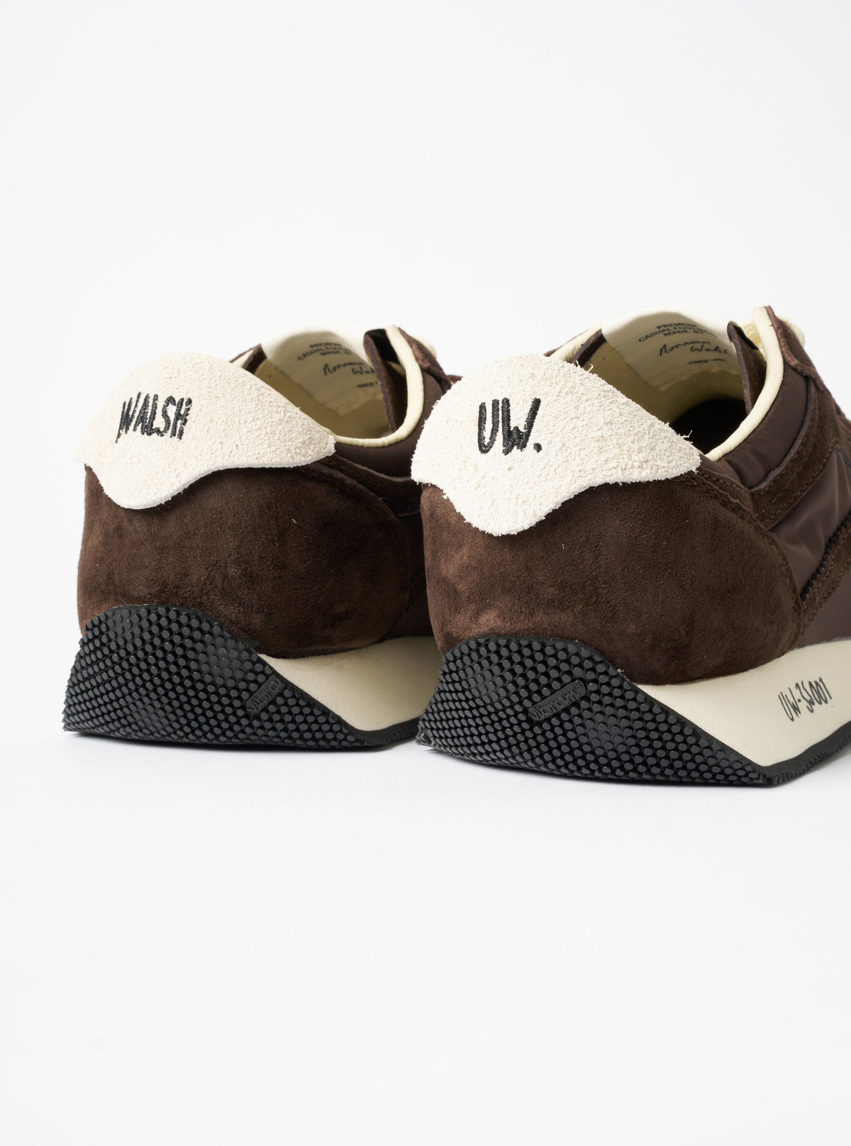 A model wearing the Walsh x Universal Works Tornado in Brown Leather/Canvas sneakers with dark trousers, captured against a clean neutral background to show the full styled look and fit.