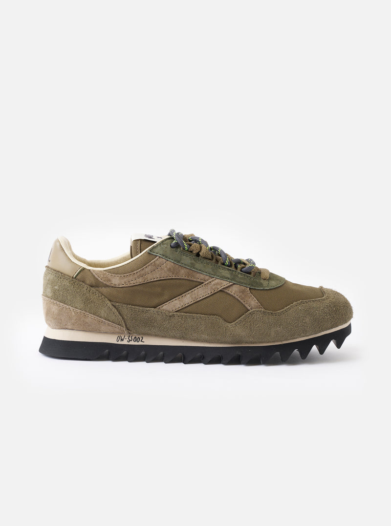 A side profile view of the Walsh x Universal Works Ensign in Green Leather/Canvas sneaker against a plain white background, displaying its green suede and canvas upper, white midsole, and hiking-inspired lace-up system.