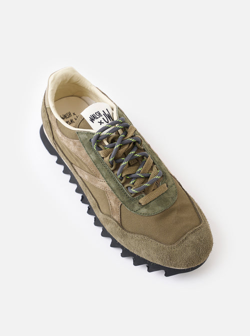 A three-quarter front angle shot of the Walsh x Universal Works Ensign in Green Leather/Canvas sneaker on a white background, highlighting the textured green paneling, reinforced toe cap, and padded collar detail.