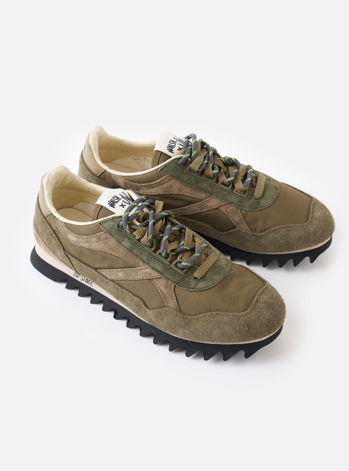 A rear view of the Walsh x Universal Works Ensign in Green Leather/Canvas sneaker positioned on a clean white background, emphasizing the structured heel tab, dual branding accents, and thick rubber tread profile.