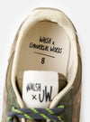 An angled view of the tread pattern on the bottom sole of the Walsh x Universal Works Ensign in Green Leather/Canvas sneaker, captured against a neutral white background to show the multi-directional traction design.