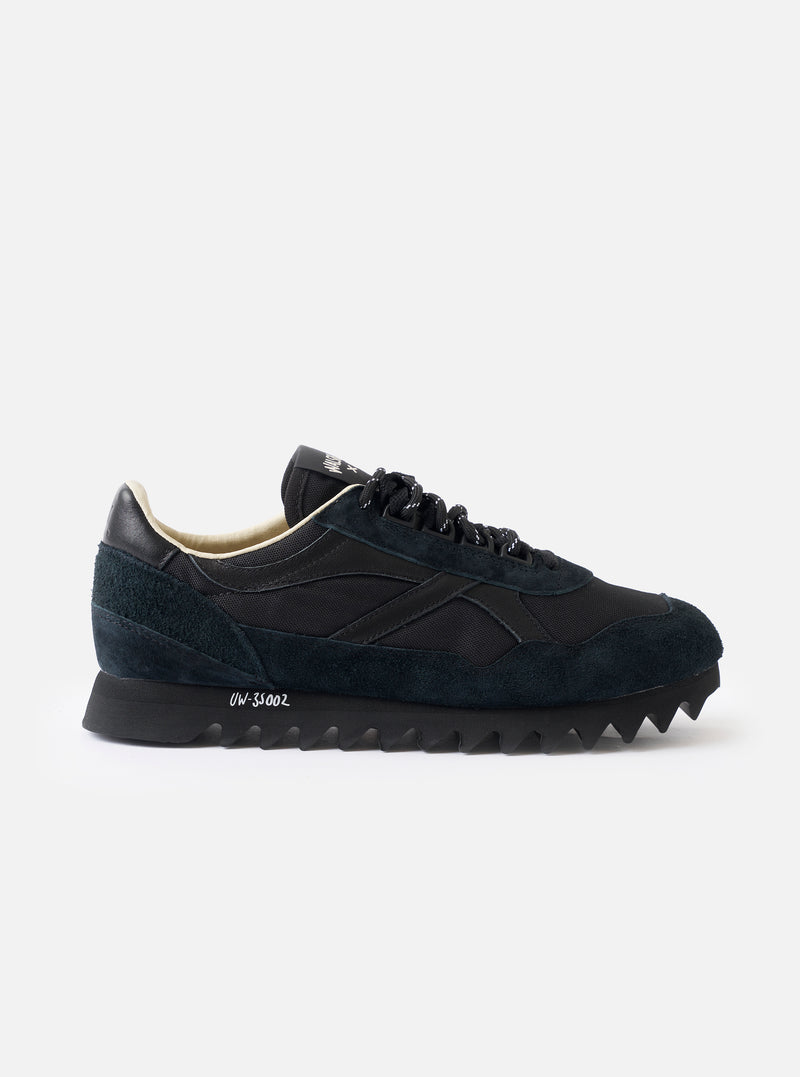 A side profile view of the Walsh x Universal Works Ensign in Black Leather/Canvas on a white background, highlighting the sleek black upper, layered leather panels, and off-white cushioned midsole.