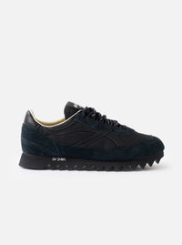 A side profile view of the Walsh x Universal Works Ensign in Black Leather/Canvas on a white background, highlighting the sleek black upper, layered leather panels, and off-white cushioned midsole.