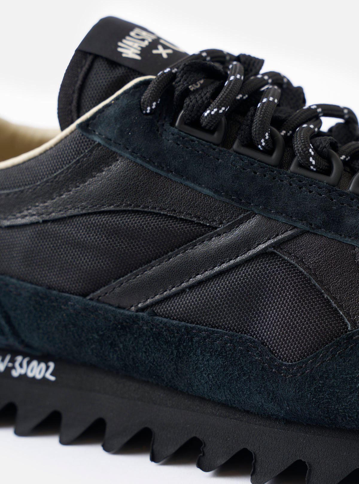 A top-down view of the Walsh x Universal Works Ensign in Black Leather/Canvas on a plain white background, featuring the black laces, branded inner soles, and rounded toe box silhouette.
