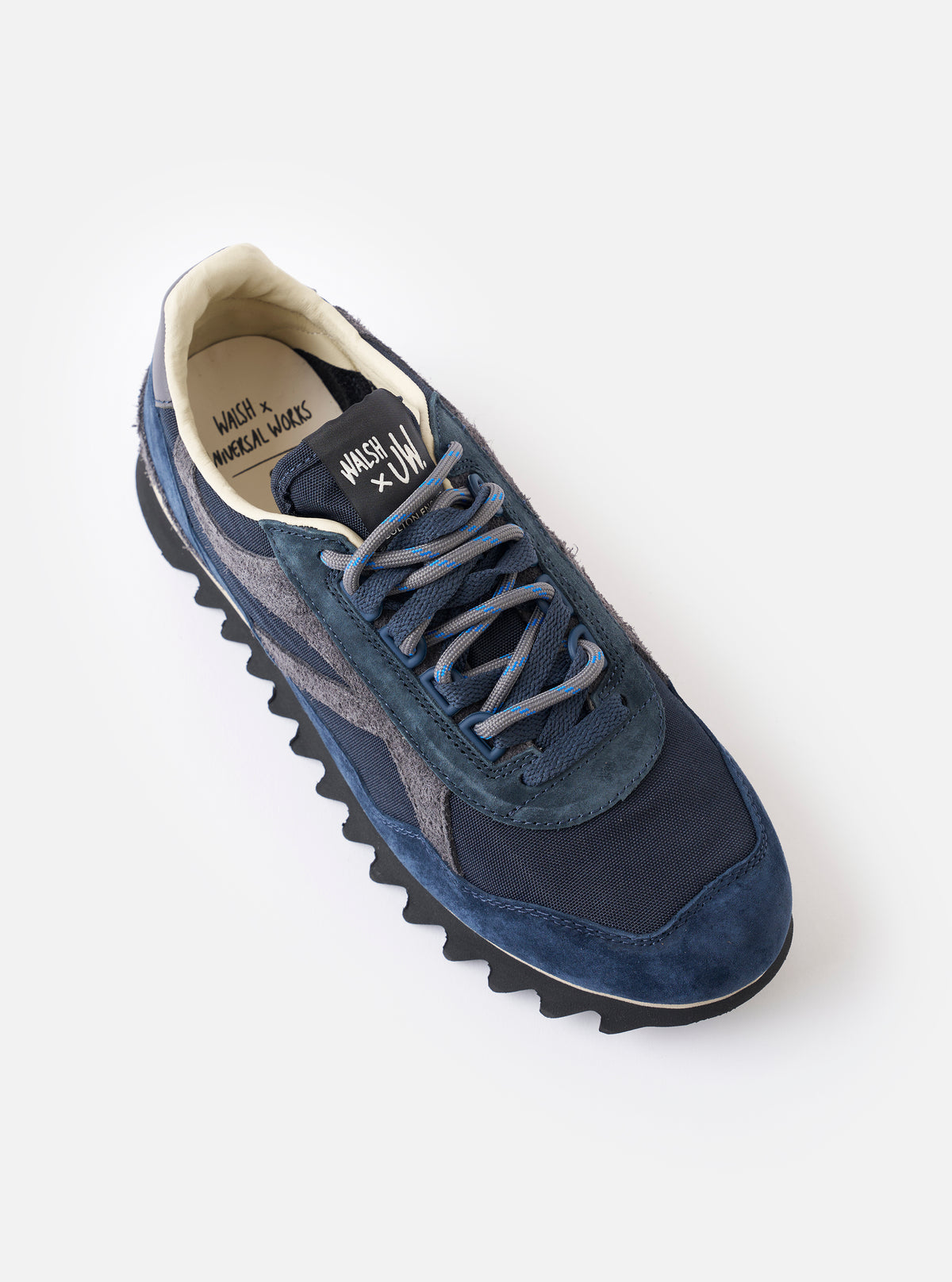 An angled pair view of the Walsh x Universal Works Ensign in Navy Leather/Canvas sneakers displayed on a solid white background, detailing the navy laces, trim, and layered upper design.