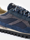 A side profile product view of the Walsh x Universal Works Ensign in Navy Leather/Canvas sneaker set against a plain white background, highlighting its navy leather and canvas panels, layered sole, and D-ring lacing design.