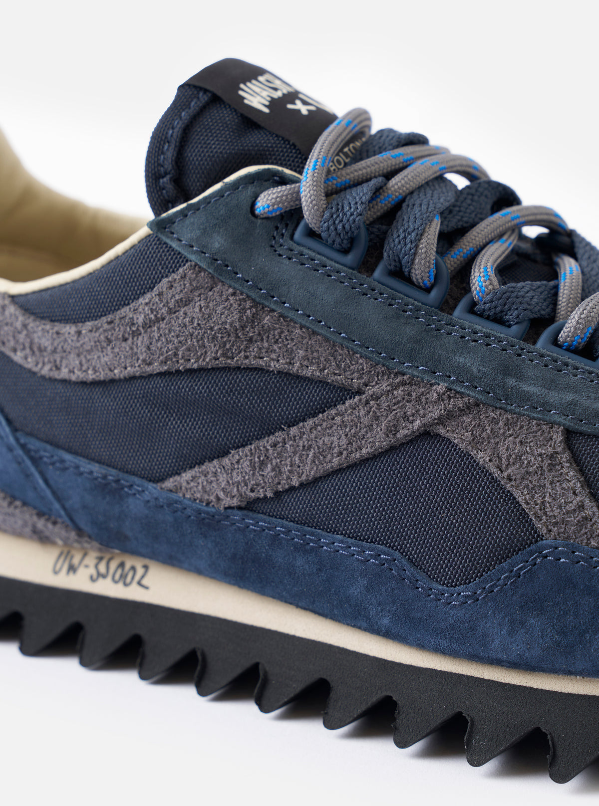 A side profile product view of the Walsh x Universal Works Ensign in Navy Leather/Canvas sneaker set against a plain white background, highlighting its navy leather and canvas panels, layered sole, and D-ring lacing design.