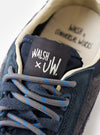 An angled view of the sole of the Walsh x Universal Works Ensign in Navy Leather/Canvas sneaker presented against a plain white background, illustrating the deep tread pattern and rugged rubber outsole design.