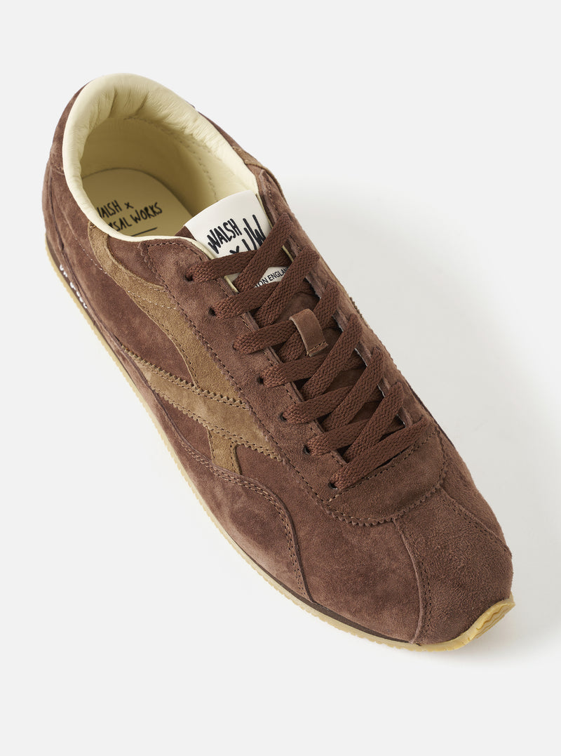A three-quarter angled front view of the Walsh x Universal Works Cob in Brown Leather trainer on a white background, highlighting the streamlined toe box, neat tonal stitching, and brown leather mudguard accents.
