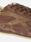 A top-down aerial view of the Walsh x Universal Works Cob in Brown Leather trainer against a plain white background, detailing the symmetry of the lace placket, soft leather lining, and minimalist internal branding.