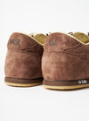 A model wearing the Walsh x Universal Works Cob in Brown Leather on foot, shown from a low angle side profile against a neutral backdrop, highlighting the shoe's low-profile silhouette and rich brown leather finish.