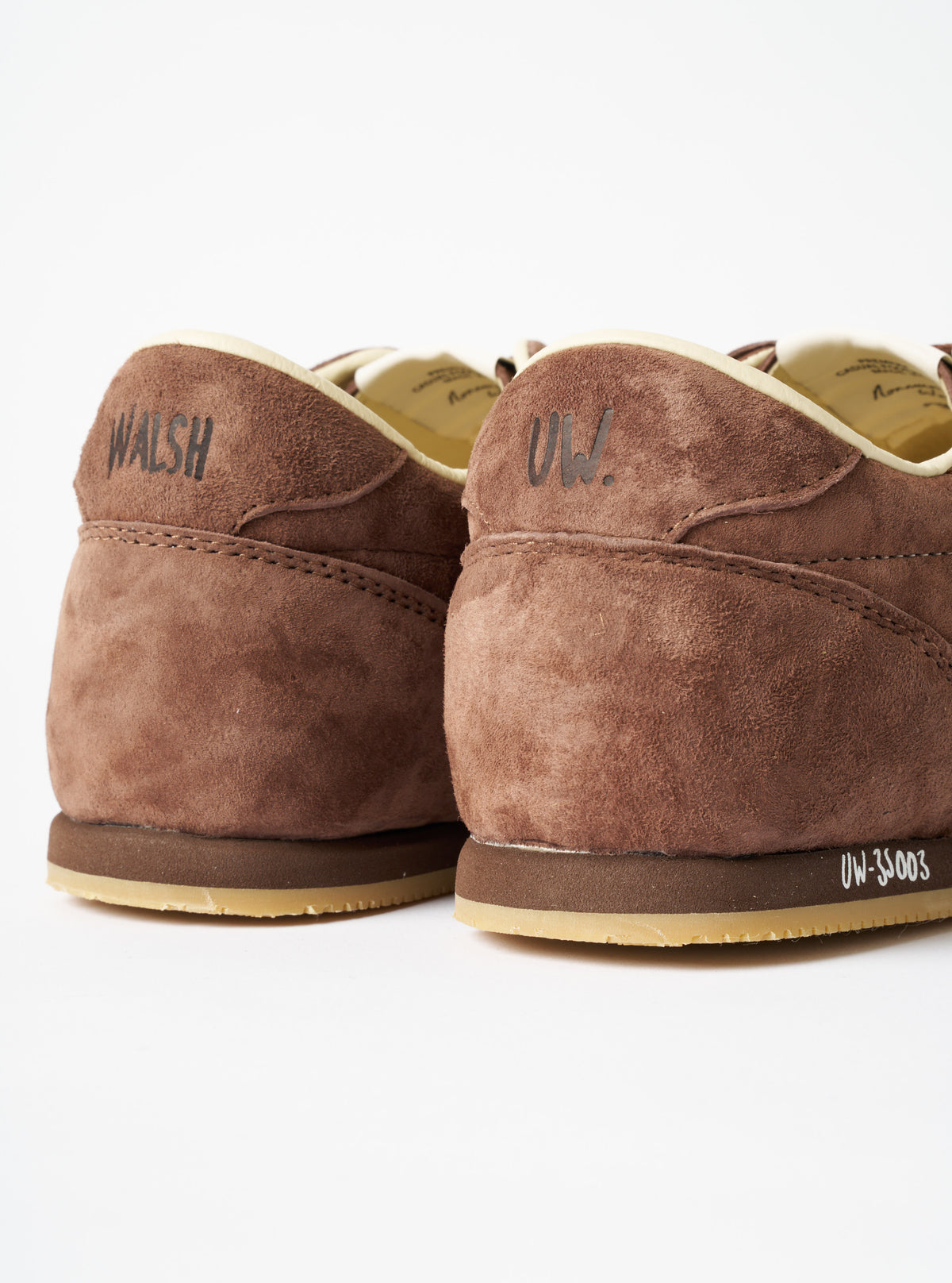 A model wearing the Walsh x Universal Works Cob in Brown Leather on foot, shown from a low angle side profile against a neutral backdrop, highlighting the shoe's low-profile silhouette and rich brown leather finish.