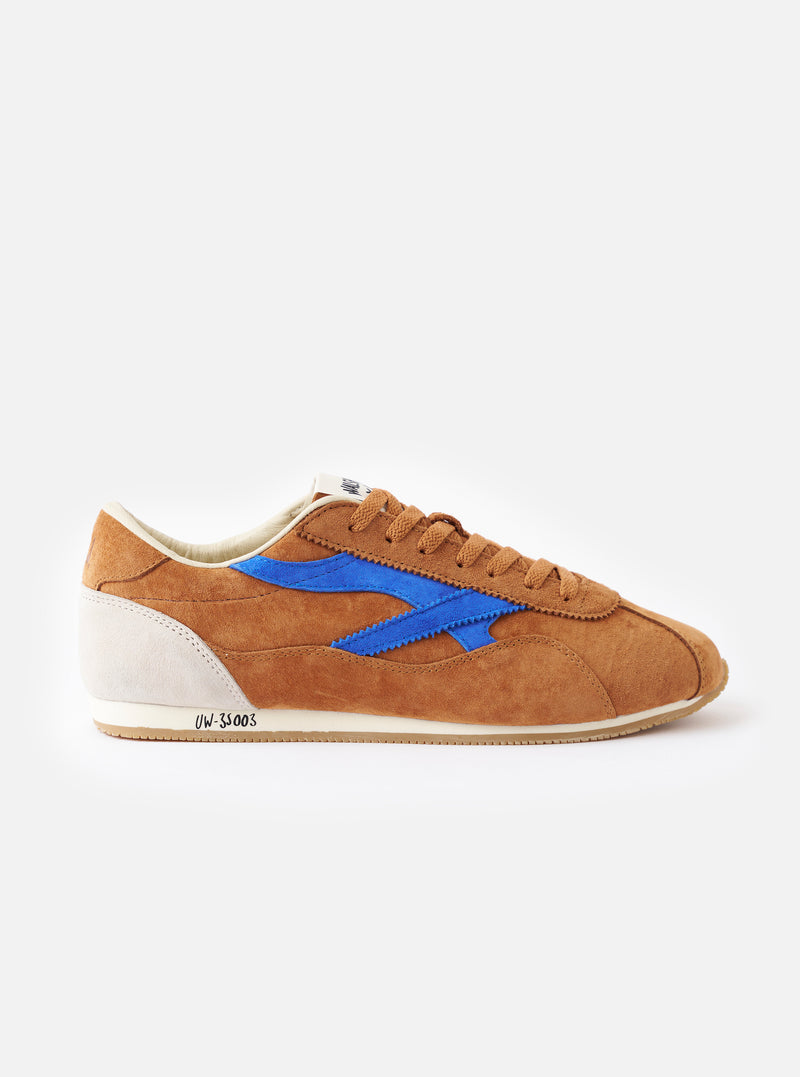 Studio product shot of the Walsh x Universal Works Cob in Tan Leather standing on a plain white surface, displaying the rich tan brown leather upper, cream sole unit, and classic low-profile design.