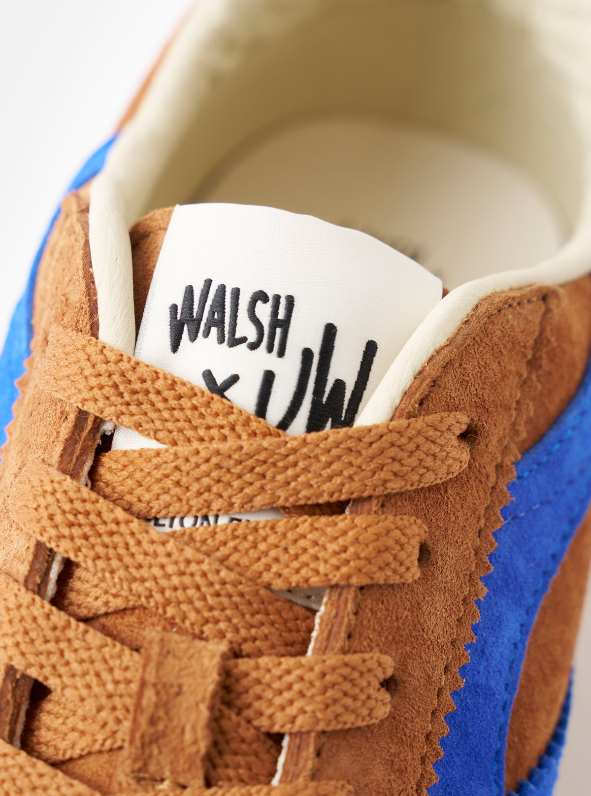 Macro detail shot of the Walsh x Universal Works Cob in Tan Leather, focusing on the fine grain finish of the tan leather, subtle debossed branding, and stitching quality on a plain background.