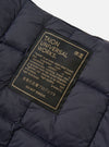 Close-up of the TAION x Universal Works Reversible Dark Navy Military Line Vest, showing the quilted texture and branded tag on a white background.