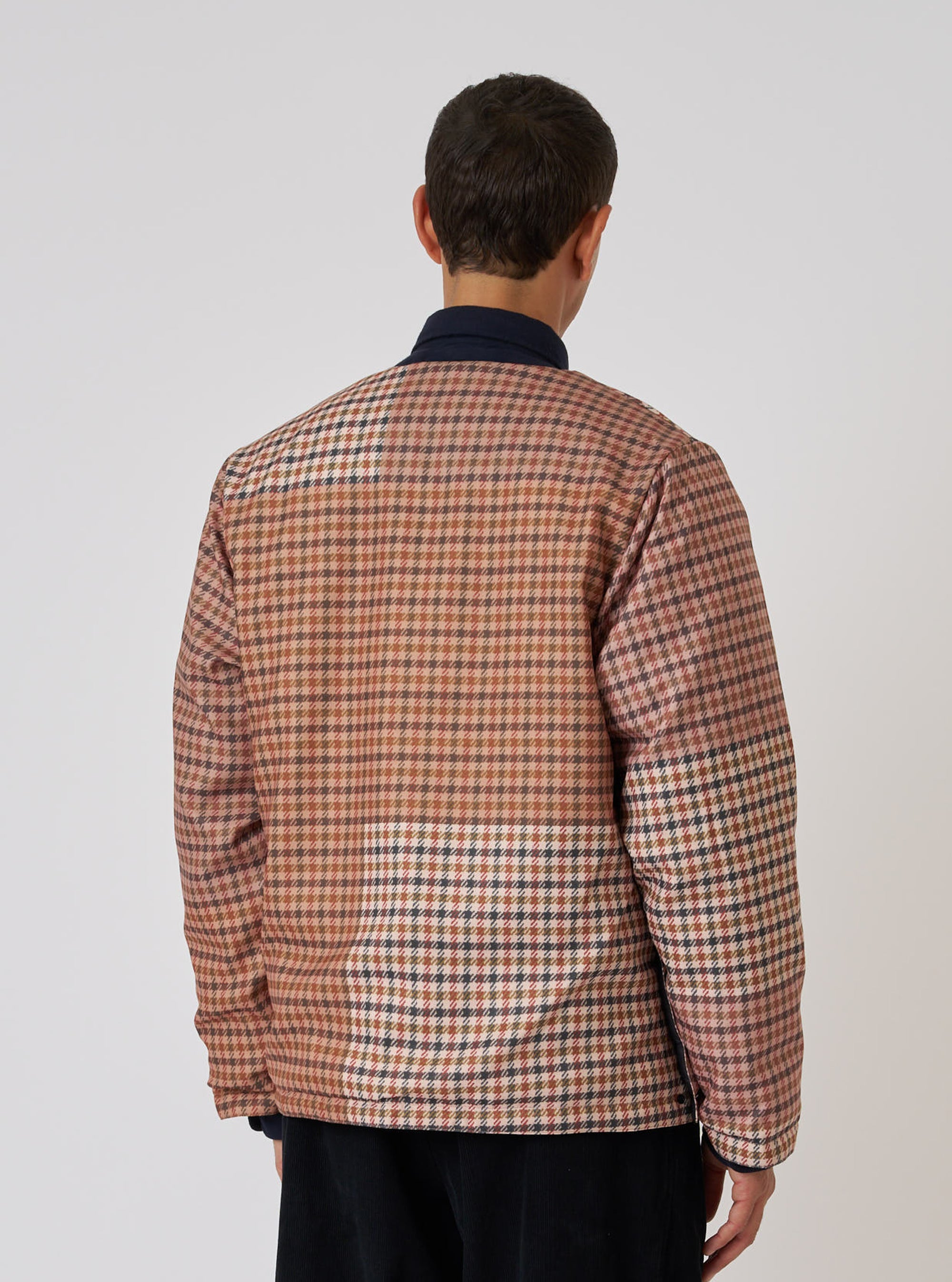 Back view of a model wearing the TAION x Universal Works Reversible Black Military Line Liner Jacket. The jacket has a brown and black houndstooth pattern. Shot against a white background.
