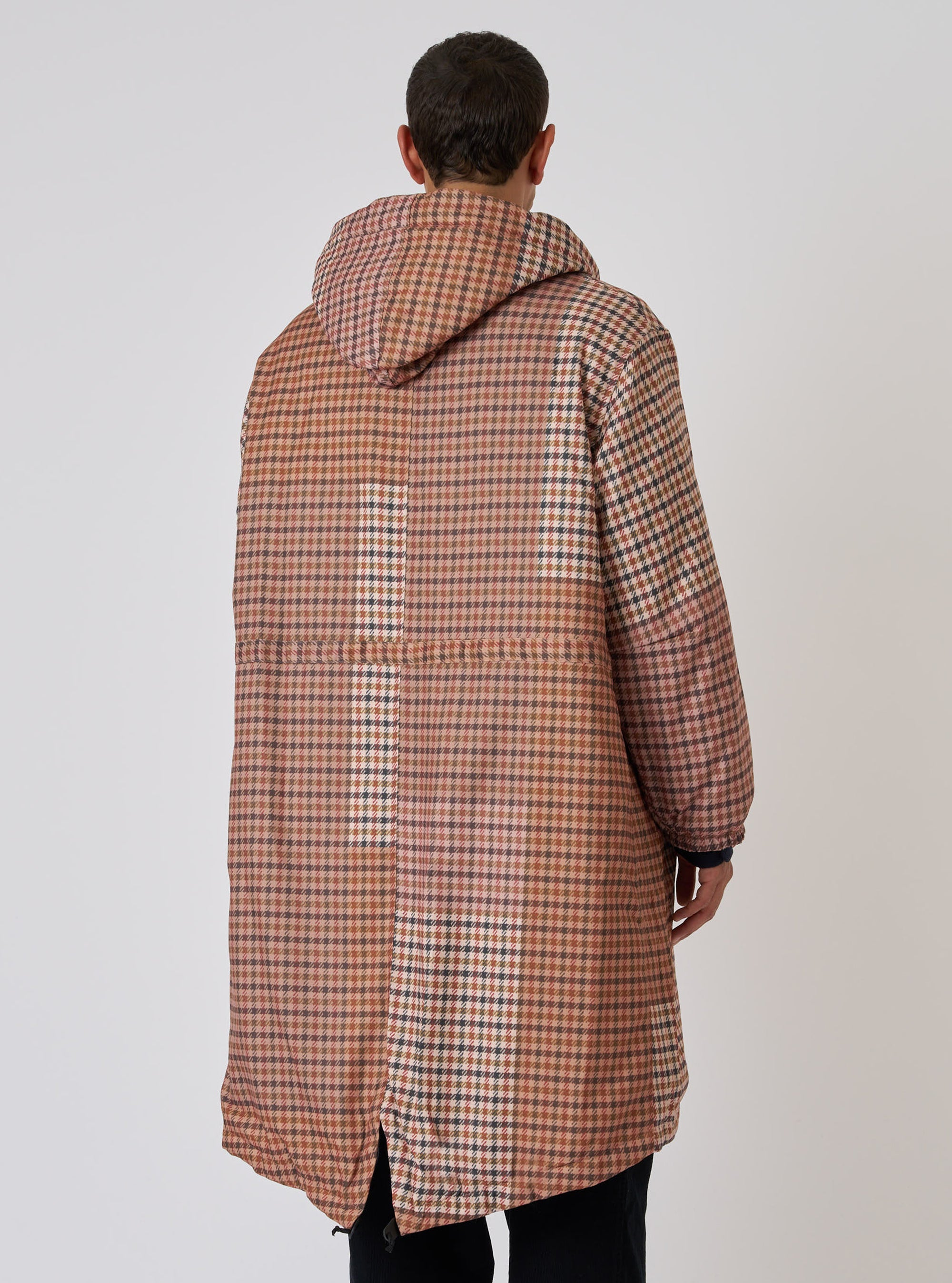 Back view of a model wearing the TAION x Universal Works Reversible Dark Olive Military Line Parka. The parka is brown and tan plaid. Shot against a white backdrop.