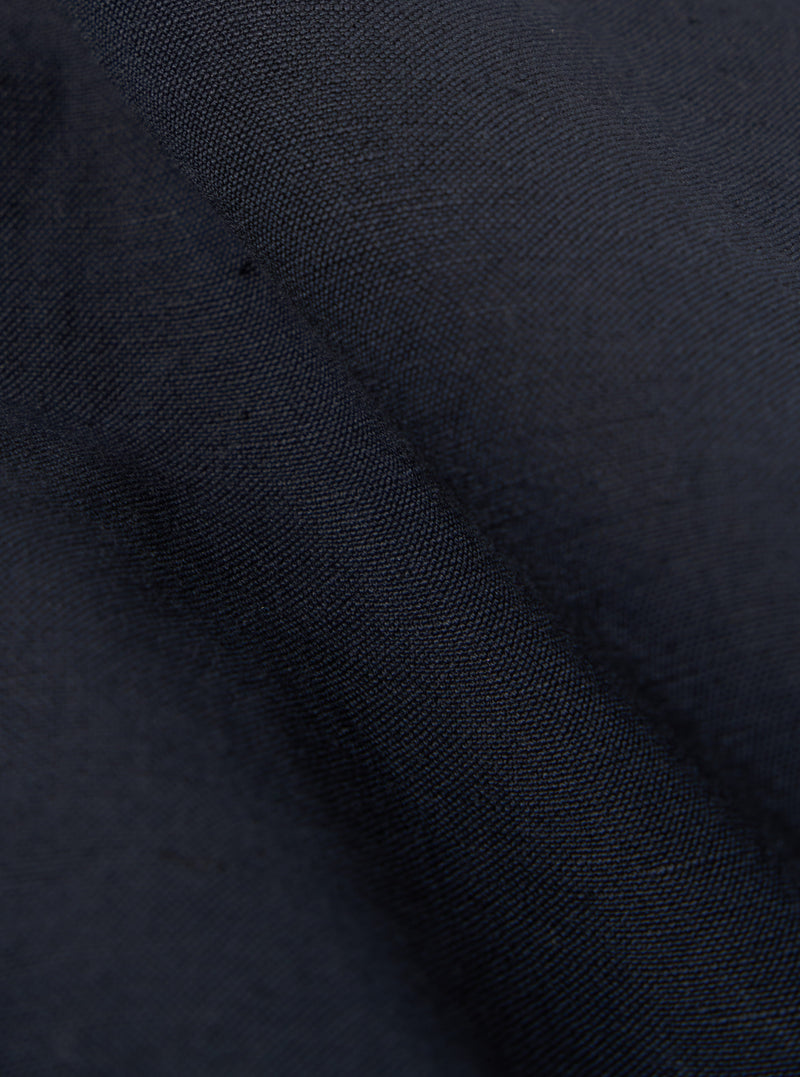 Close-up of the navy linen slub weave Bakers Jacket fabric, showing the texture and color. The material is folded, creating shadows and highlights.
