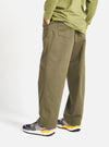 A person stands against a white backdrop, showcasing the Light Olive Twill Duke Pant. The pants, made of twill, have a relaxed fit. They are paired with sneakers and a matching shirt.