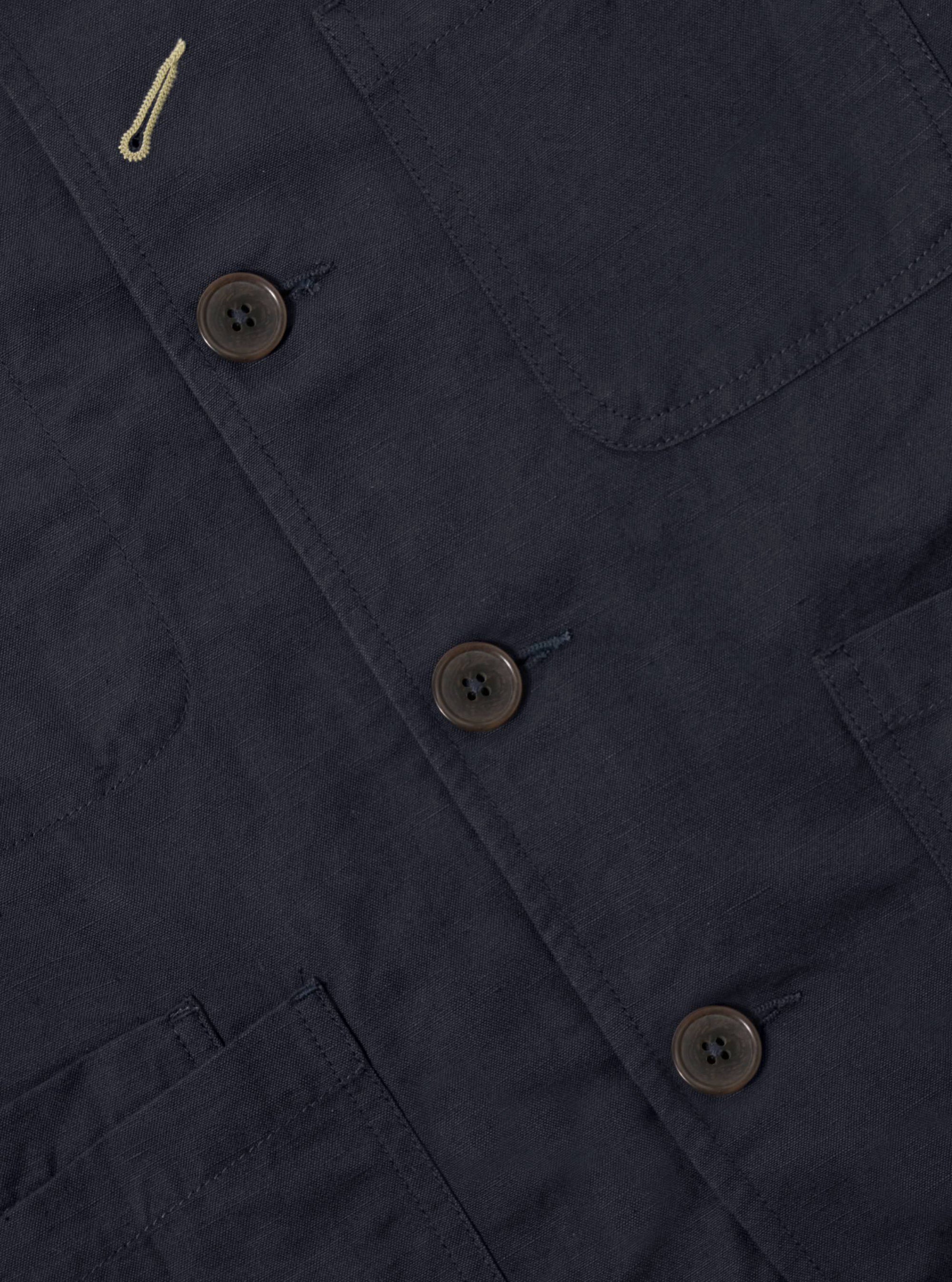 Close-up of the Navy Linen Slub Weave Bakers Jacket showing the linen texture, button details, and pocket stitching. The jacket is laid flat on a neutral surface.