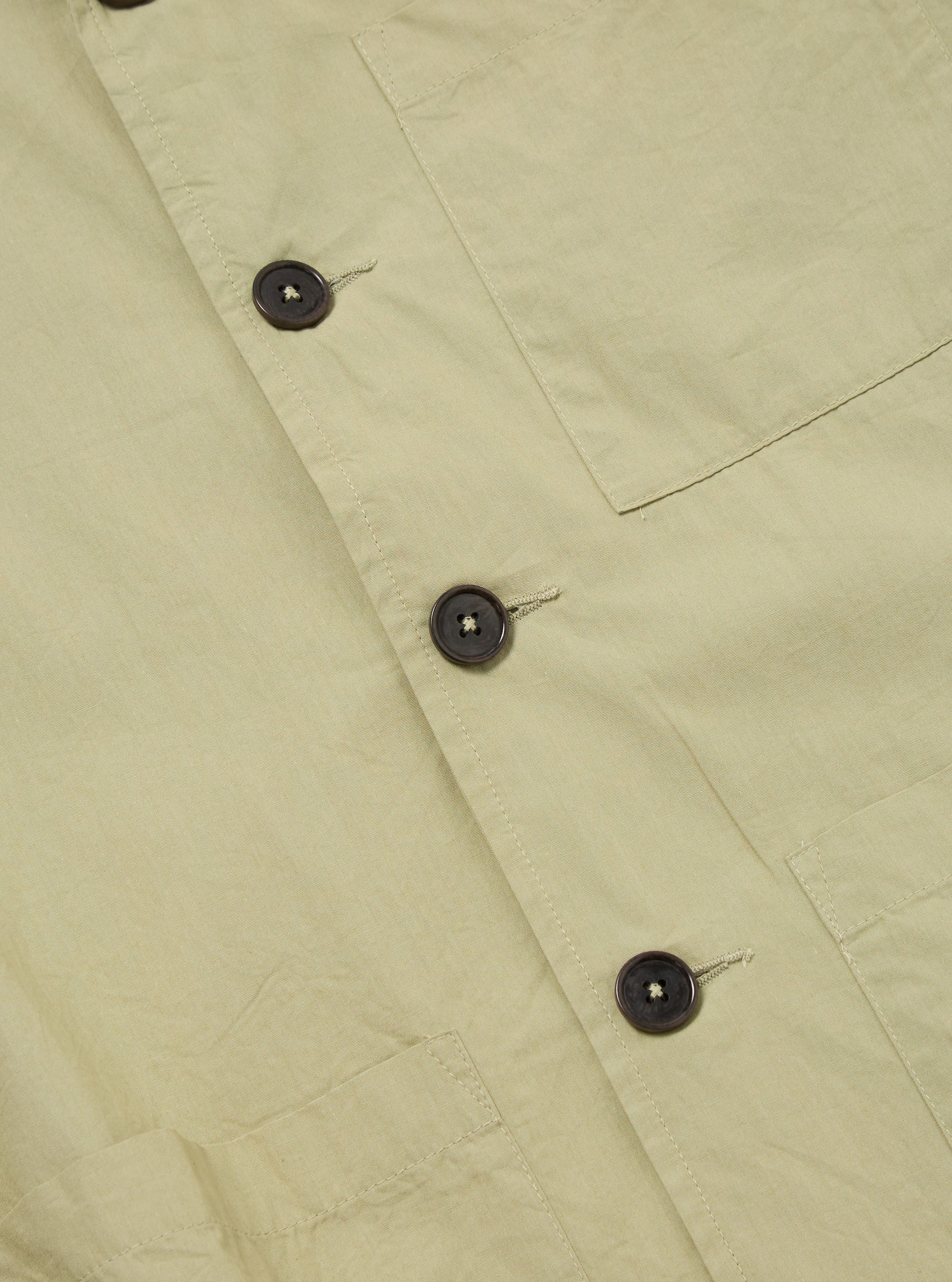 Close-up of the pale green Broadcloth Cancun Jacket. The jacket is made of broadcloth material and features brown buttons. The background is a plain white surface.