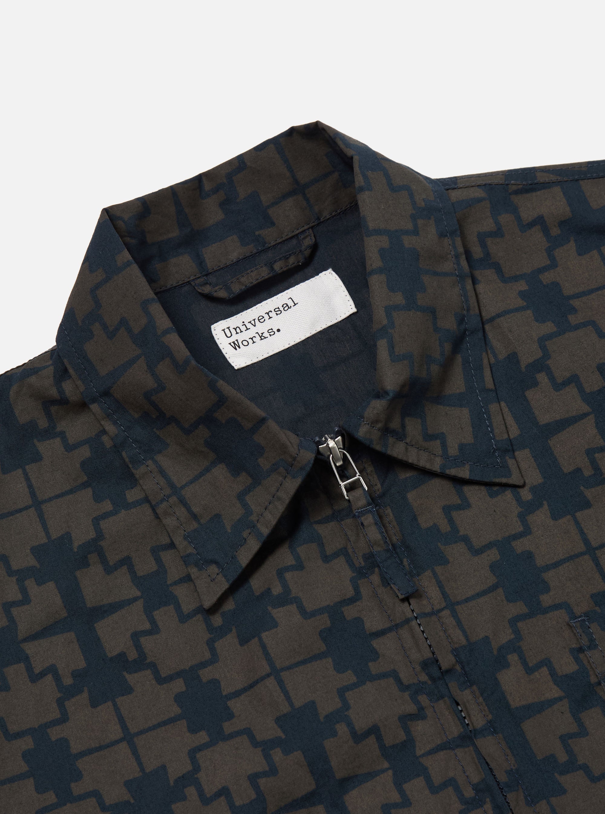 Close-up of the Navy Mitla Print Cotton Rose Bowl Jacket. The jacket features a navy and brown geometric print, a full zip, and is made of cotton. Shot on a white background.