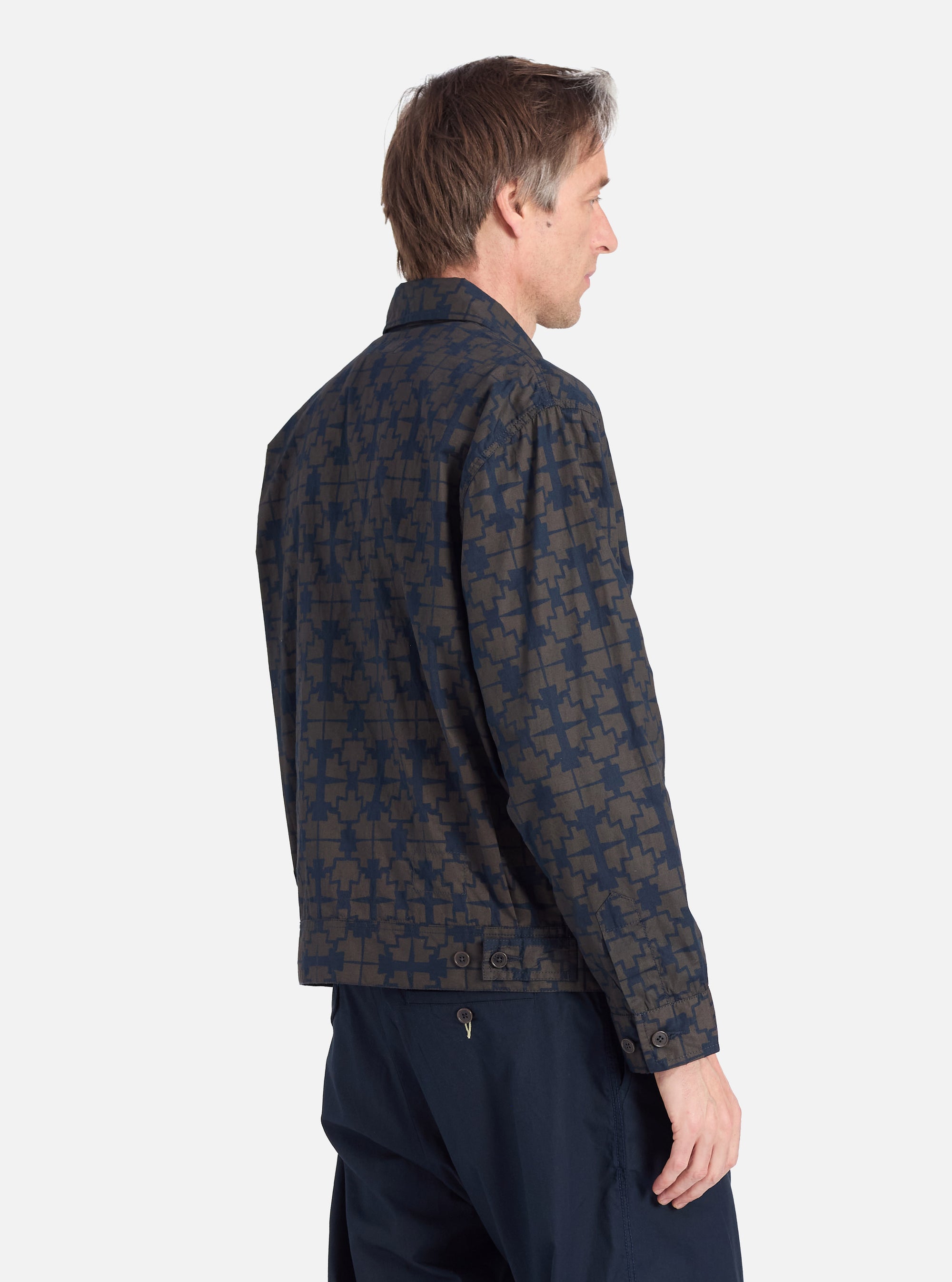 A man models the Navy Mitla Print Cotton Rose Bowl Jacket in a studio shot against a white background. The jacket features a navy and brown geometric print.