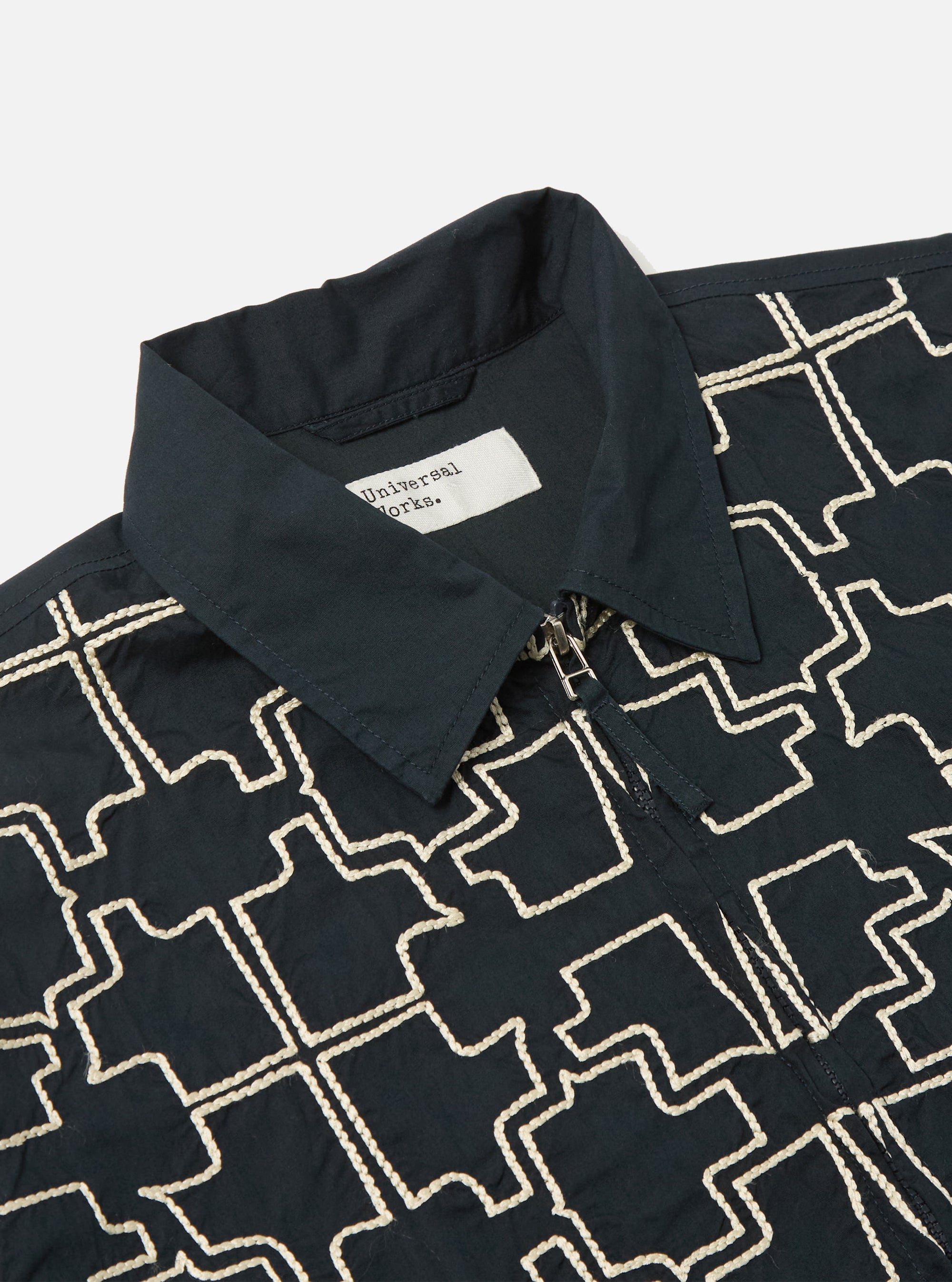 Close-up of the Navy Mitla Broadcloth Club Jacket on a white surface. The jacket is navy with a white geometric pattern and a silver zipper.