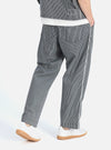 Model wearing Indigo Hickory Stripe Denim Duke Pant in studio. The relaxed-fit pants are blue and white striped denim. Worn with white sneakers. 