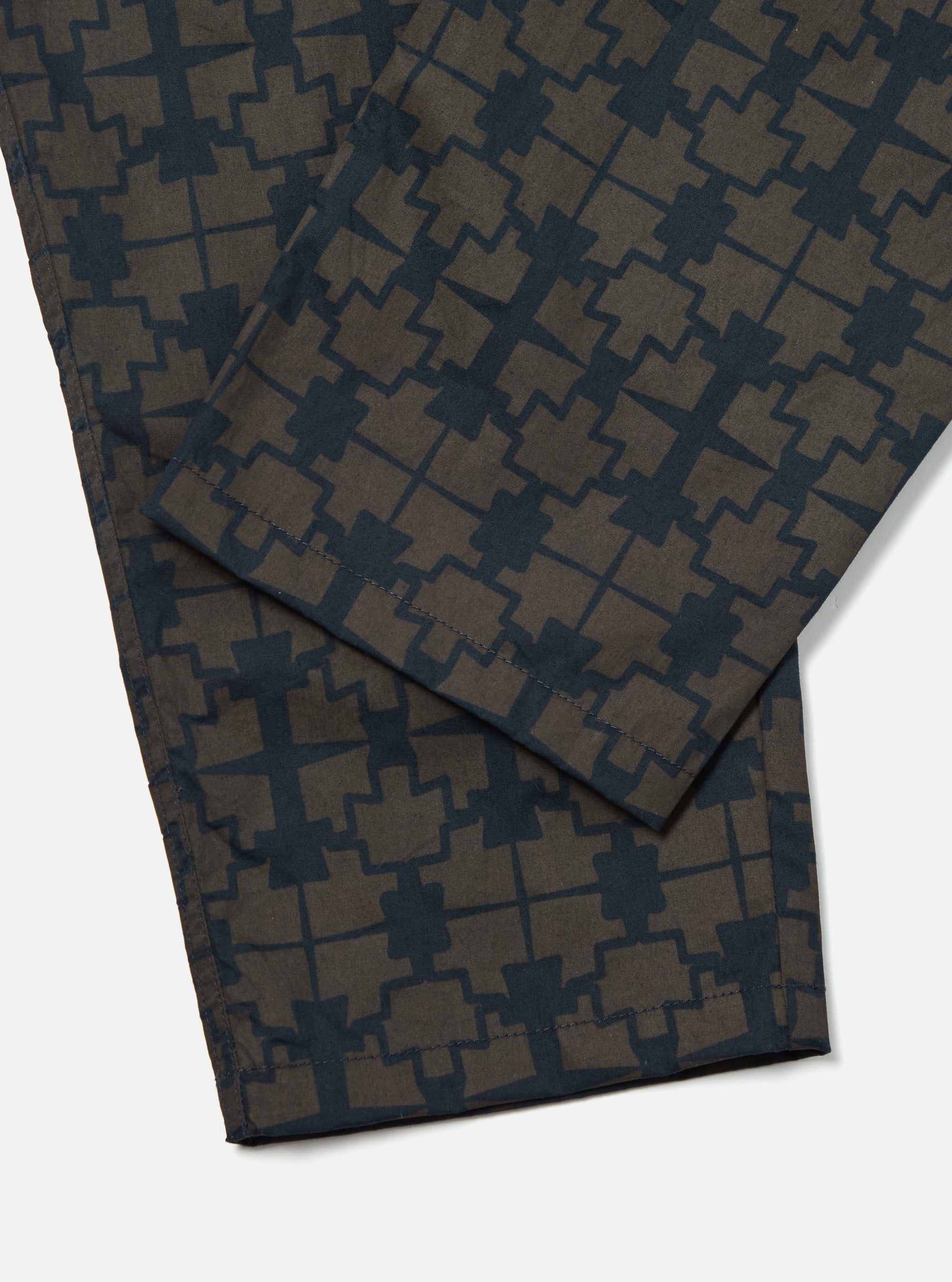 Close-up of the Navy Mitla Print Cotton Hi Water Trouser on a white surface. The cotton trousers feature a navy geometric print on a brown base.