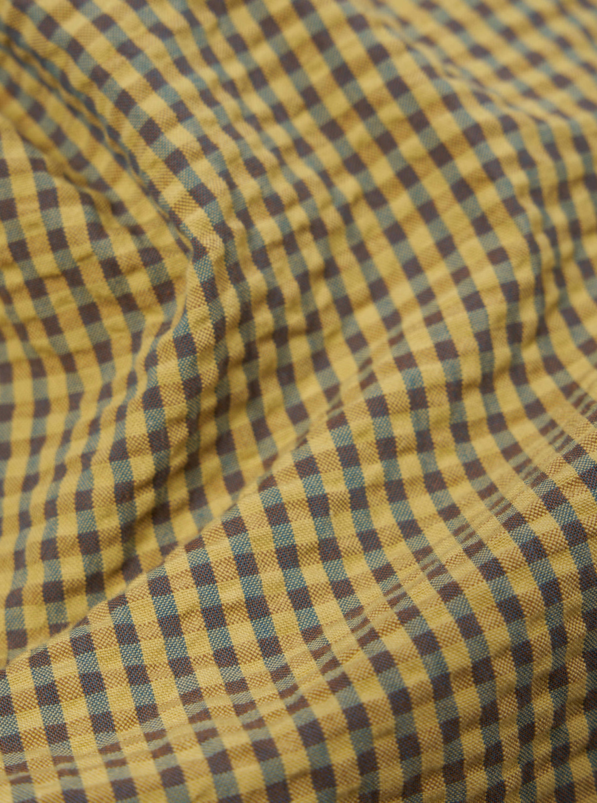 Close-up of the Yellow Japanese Seersucker Pleated Track Short fabric. The material is a yellow and blue plaid with a textured seersucker feel.