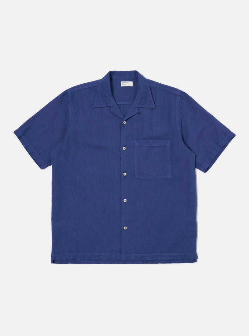 The Blue Linen Cotton Shirting Camp Shirt is laid flat on a white background. The shirt is a solid blue, short sleeved, and has a pocket on the right breast.