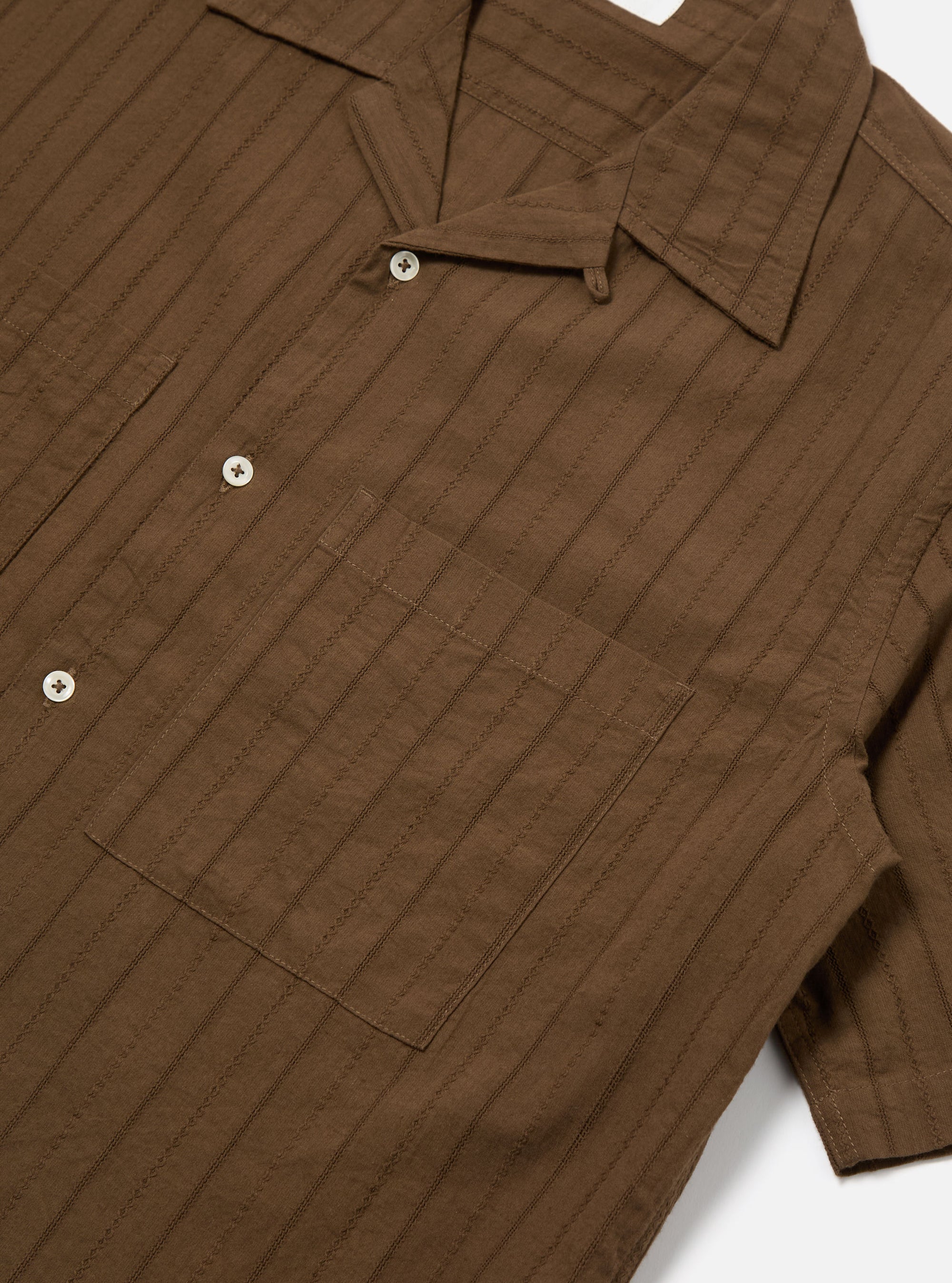 Close-up of the Brown Dobby Self Stripe Camper Shirt on a white surface. The shirt is brown with a subtle stripe pattern and features a chest pocket and short sleeves.